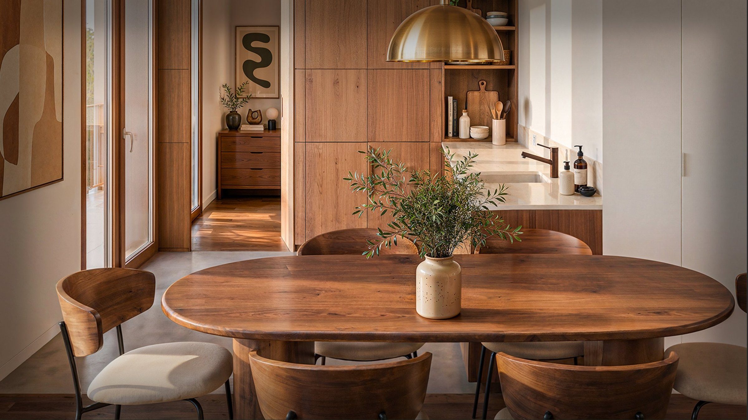 La cuisine du duplex A61 : placage de noyer, plan de travail en pierre claire, table ovale au premier plan.