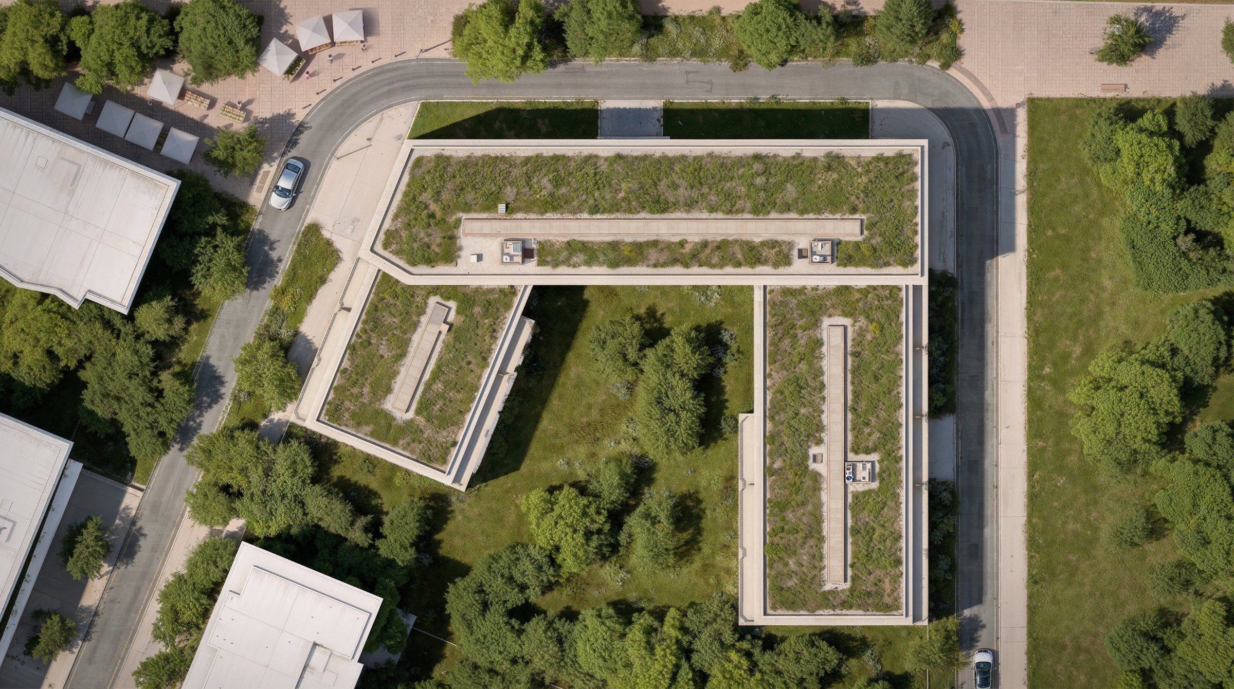 Plan de masse vu du ciel : trois ailes en U autour d’un jardin planté, halls A, B et C, R+5 au sud et R+7 au nord, l’allée des Casemates au nord et le parc à l’est.